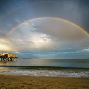 A vibrant double rainbow arcs over Old Orchard Beach, with sunlight reflecting on the sand and water, symbolizing hope and beauty in nature.