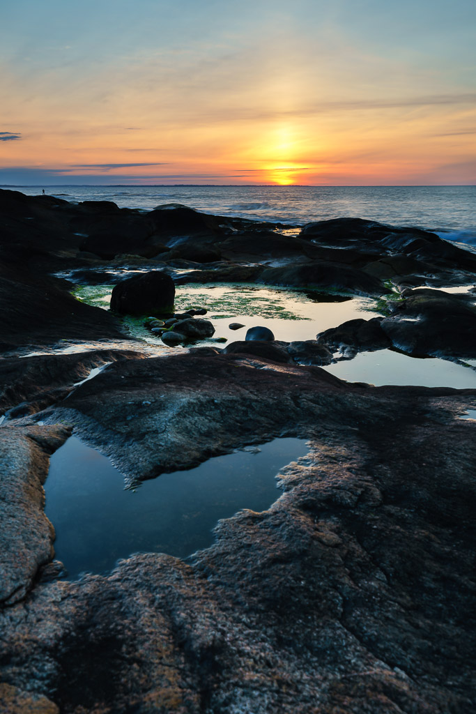 Rocky coastline at sunrise along Narragansett Bay with a heart-shaped tide pool in the rocks and soft golden light through low clouds